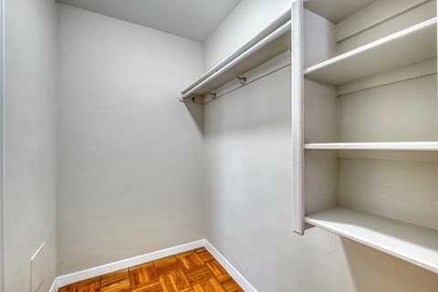 an empty closet with white shelves and wood flooring